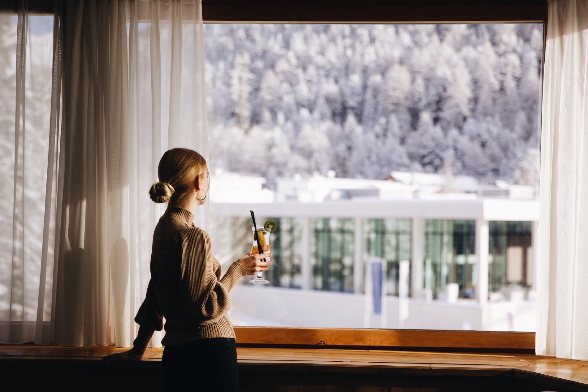 A guest with a drink at a window over the snow-frosted valley.