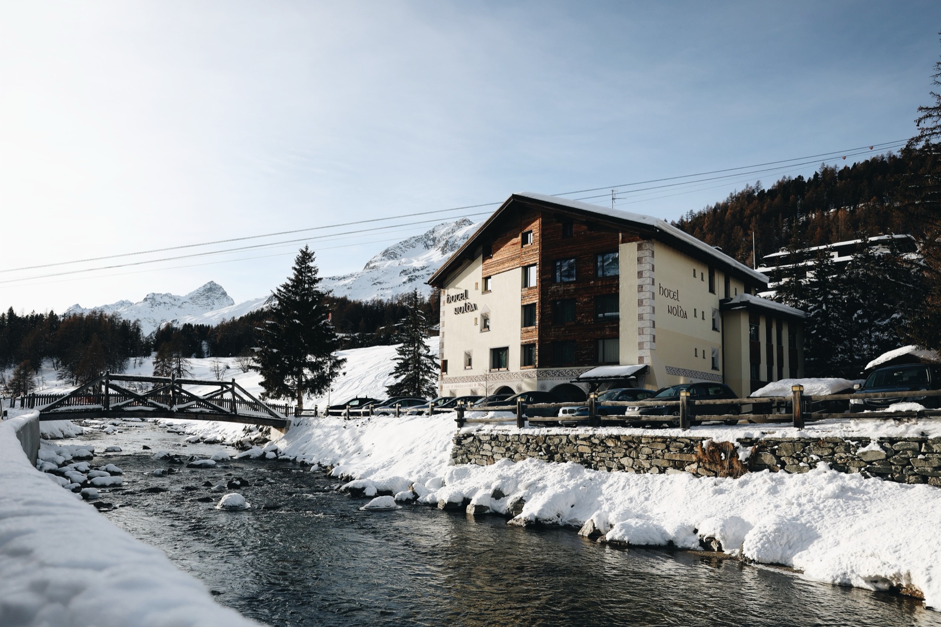 Hotel Nolda beside the river, framed by snow-covered peaks.