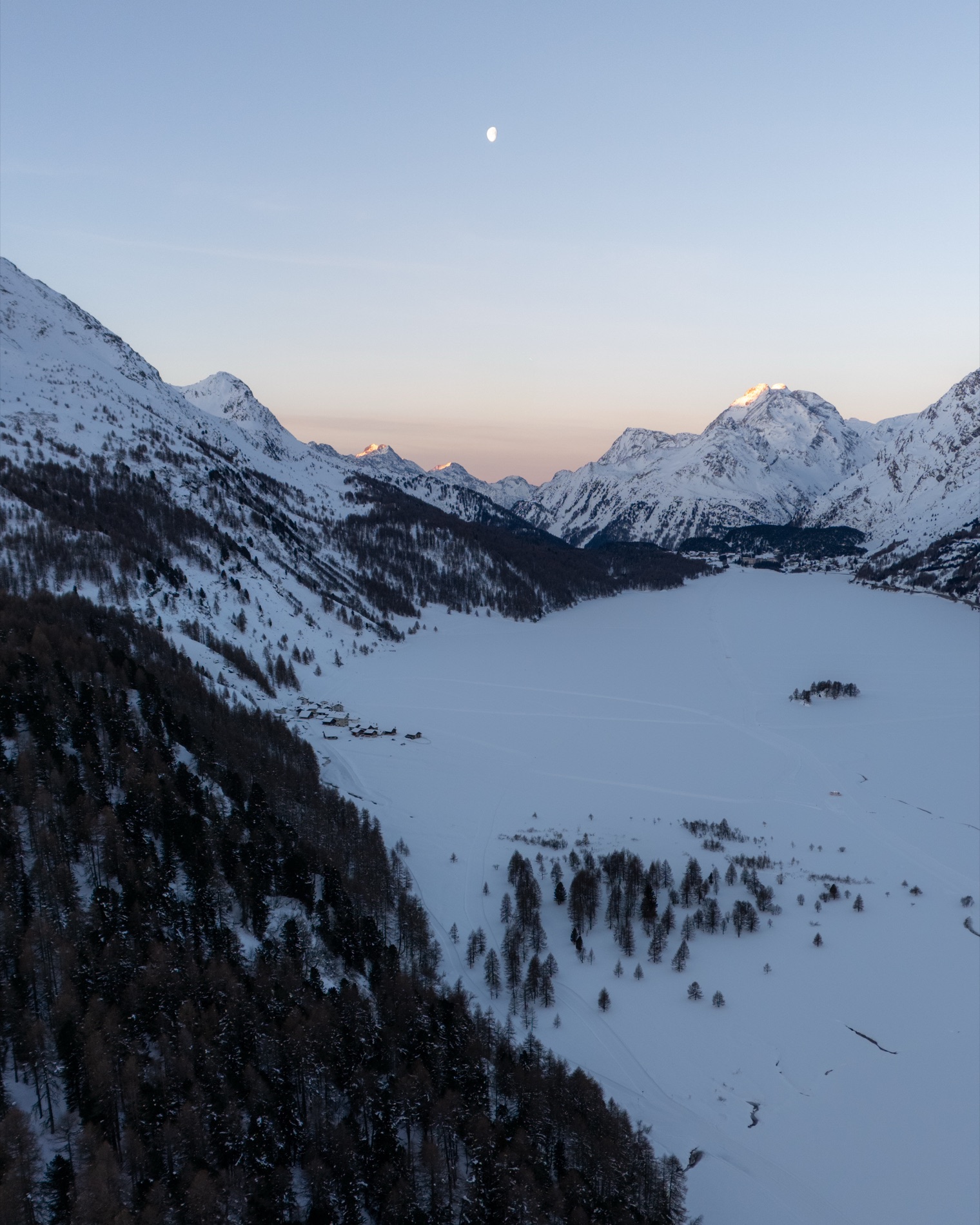 A snow-covered Engadin valley at dusk under a rising moon.